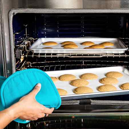 Person using blue pot holder to remove a tray of cookies from the oven.
