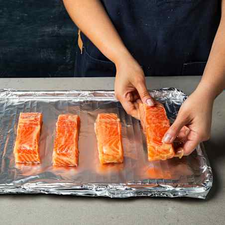 Person placing four pieces of salmon on baking sheet lined with aluminum foil