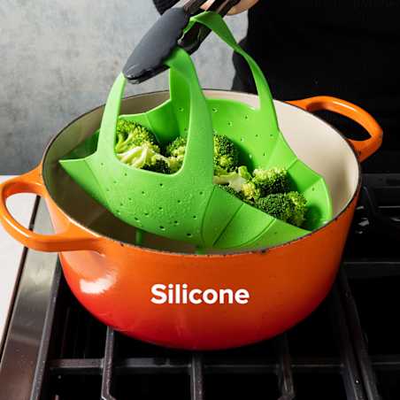 a person lifts a green silicone steamer basket full of dumplings by grabbing the two silicone handles using a pair of tongs. 