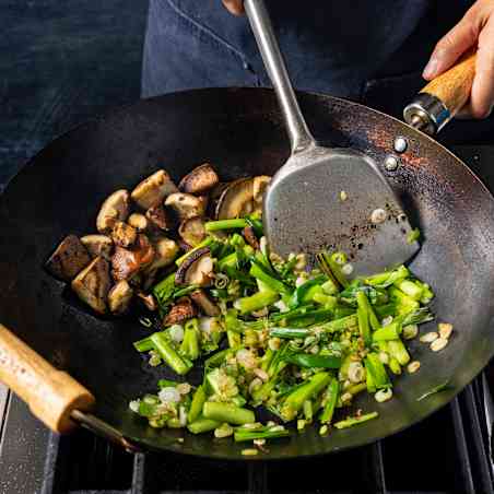 Greens and mushrooms are stir-fried in a wok using a special wok spatula.