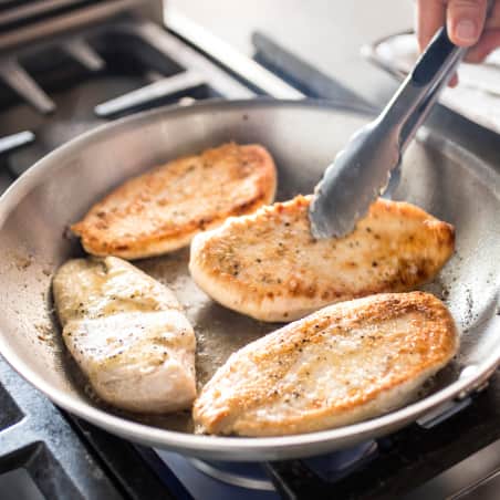 Skillet with four golden brown boneless skinless chicken breasts