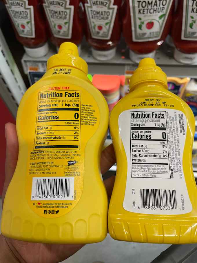 hand holding two mustard bottles with the nutrition labels facing forward.