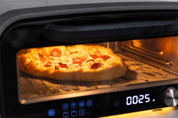 Pepperoni pizza cooking in Ooni pizza oven, with timer reading 00:25.