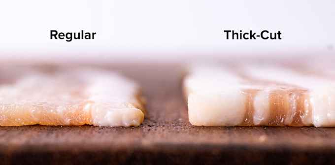 Slices of raw regular and thick-cut bacon side-by-side on a wood cutting board.