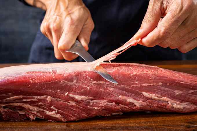 A boning knife is used to remove the silverskin from a tenderloin.