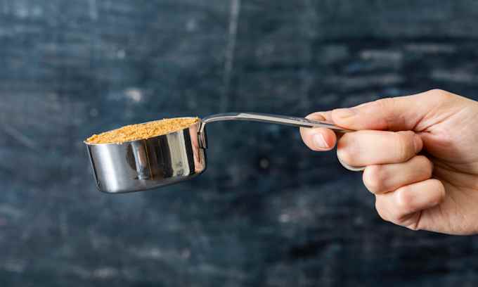 A measuring cup filled with wet sand with a handle that’s bent downward