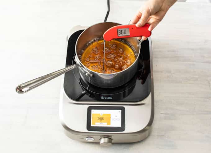 A saucepan of sugar and water caramelizes on an induction burner, while we check its temperature with a separate thermometer.
