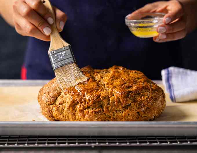 Wood-handled pastry brush brushing melted butter onto Irish soda bread.