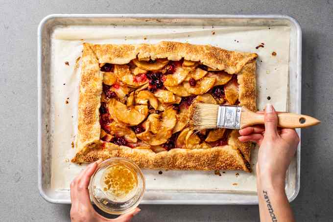 Wood-handled pastry brush brushing preserves onto a fruit tart.