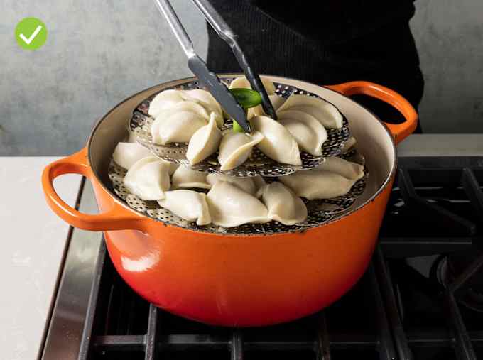 a metal collapsible steamer basket with broccoli florets inside in an orange Dutch oven. 