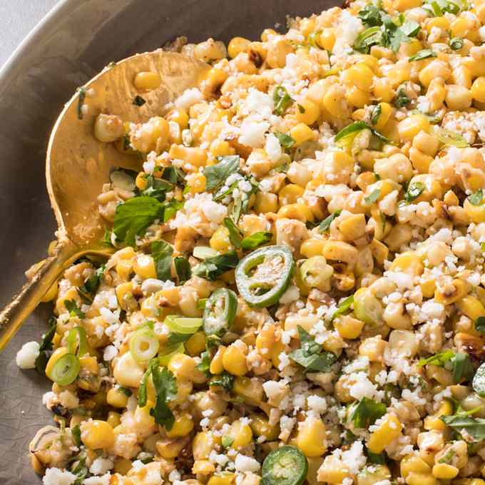 A bowl of corn salad with a serving spoon in it