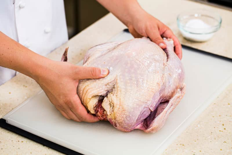 someone holding a raw turkey on a cutting board