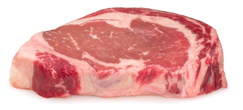 A raw rib-eye steak, showing the two clear parts divided by fat. 