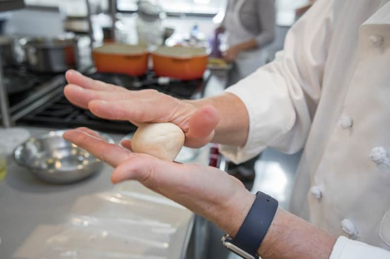 Hands rolling a dough ball together.