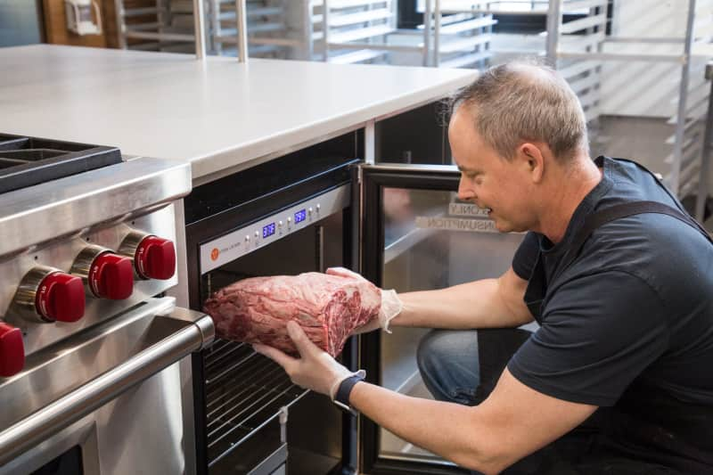 Steve Dunn placing meat in a refrigerator designed for dry aging in the test kitchen.