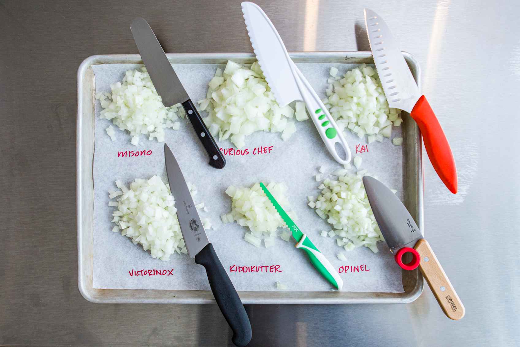 Overhead shot of six piles of diced onions with six chef’s knives for kids next to the piles.