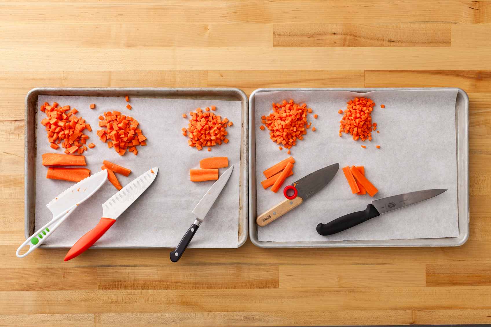 Overhead shot of diced carrots sitting on parchment paper in a sheet tray. Five chef’s knives for kids are also visible. 