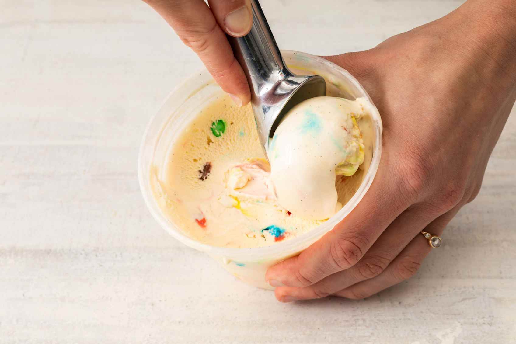 Person scooping vanilla ice cream with colorful M&Ms.