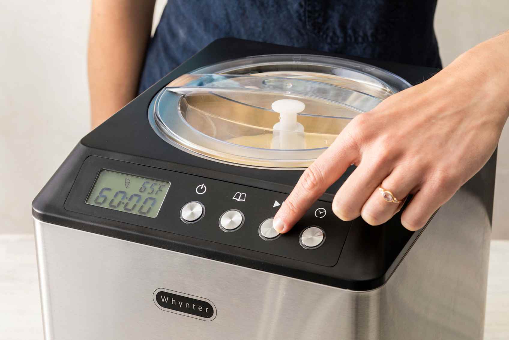 Person pressing the on button on a silver and black ice cream maker.