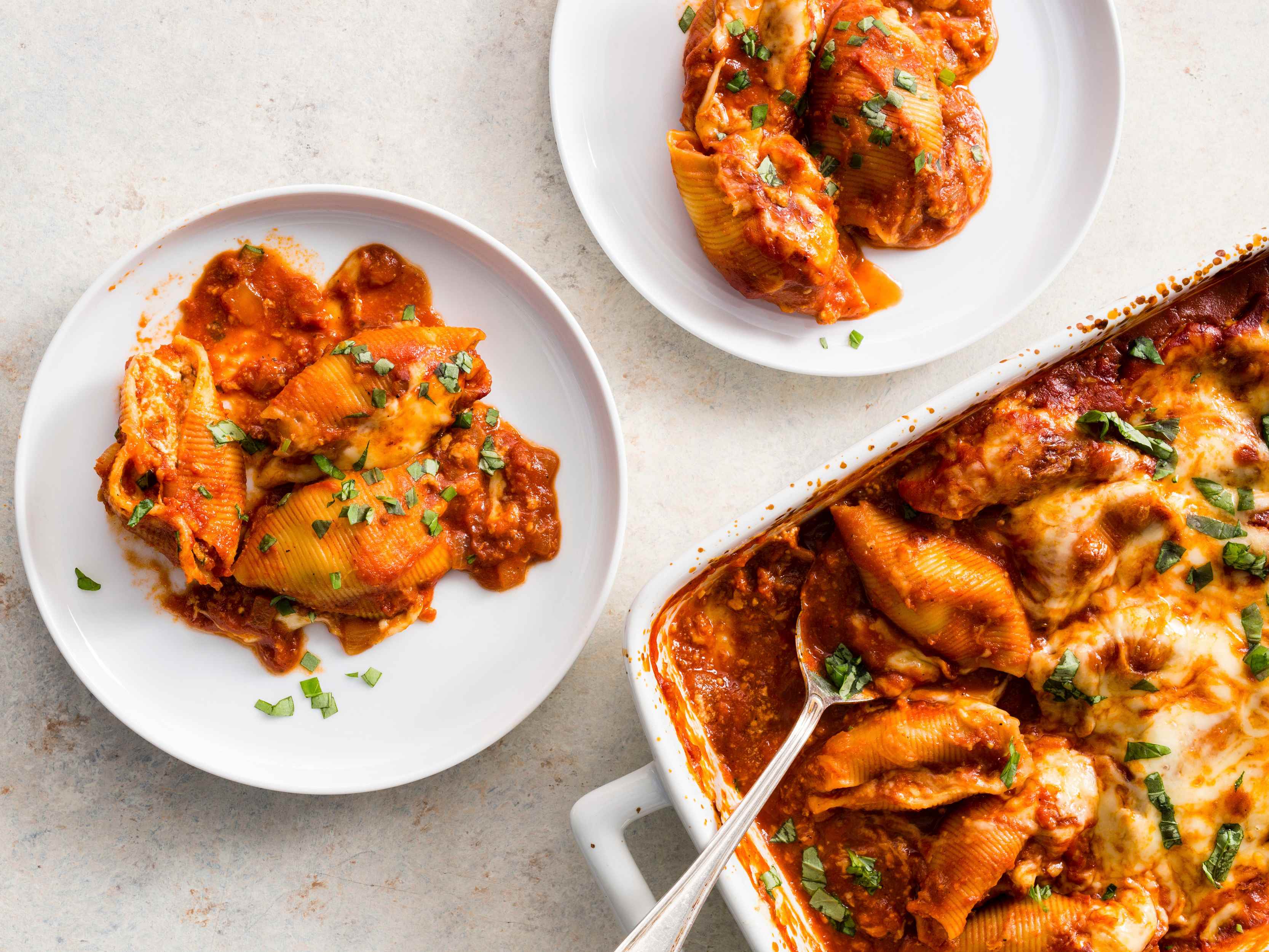 Two servings of Cheesy Stuffed Shells are portioned onto white plates next to the whole casserole