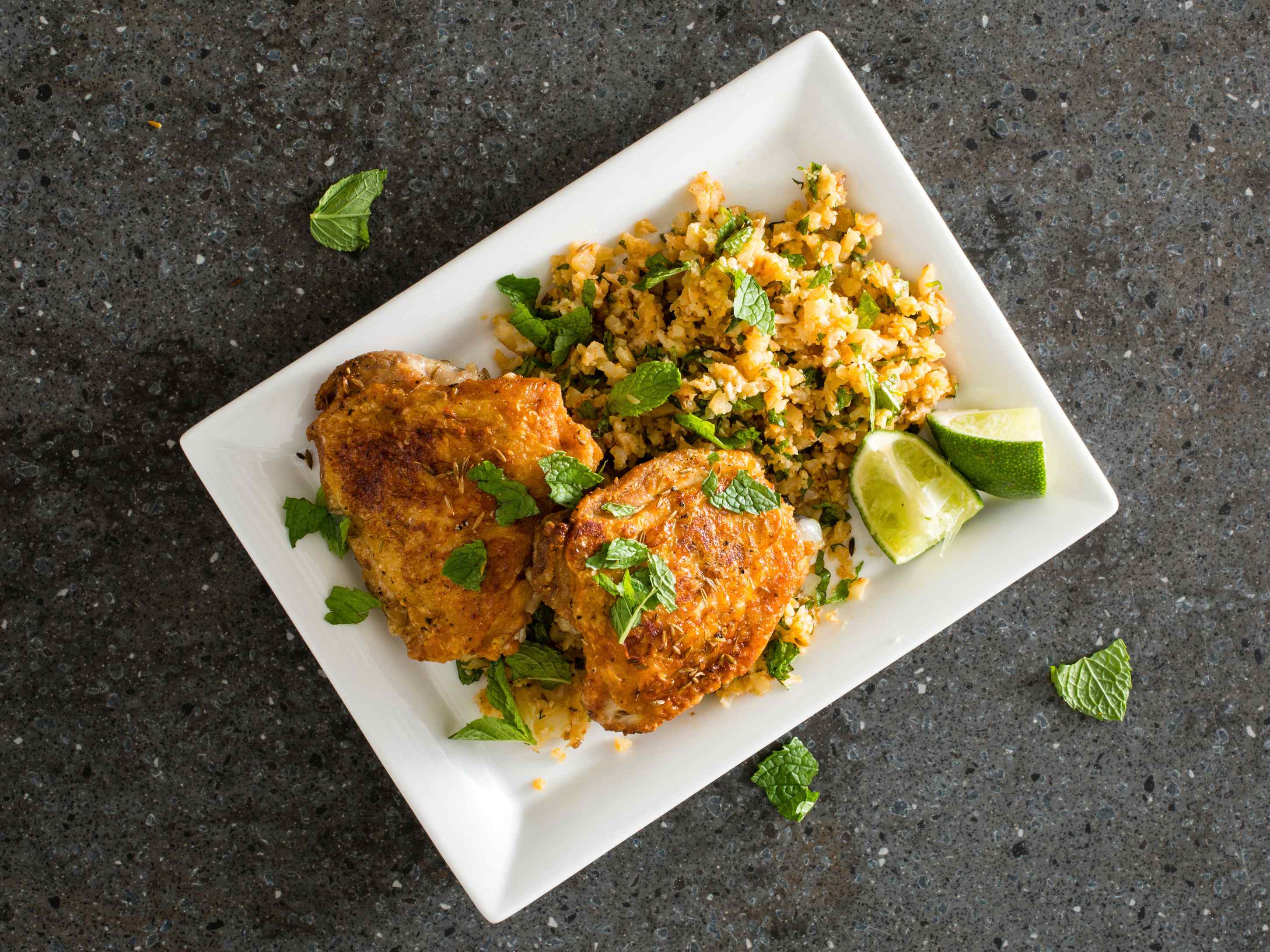 Cumin-Crusted Chicken Thighs with Cauliflower “Couscous” on a white rectangular plate