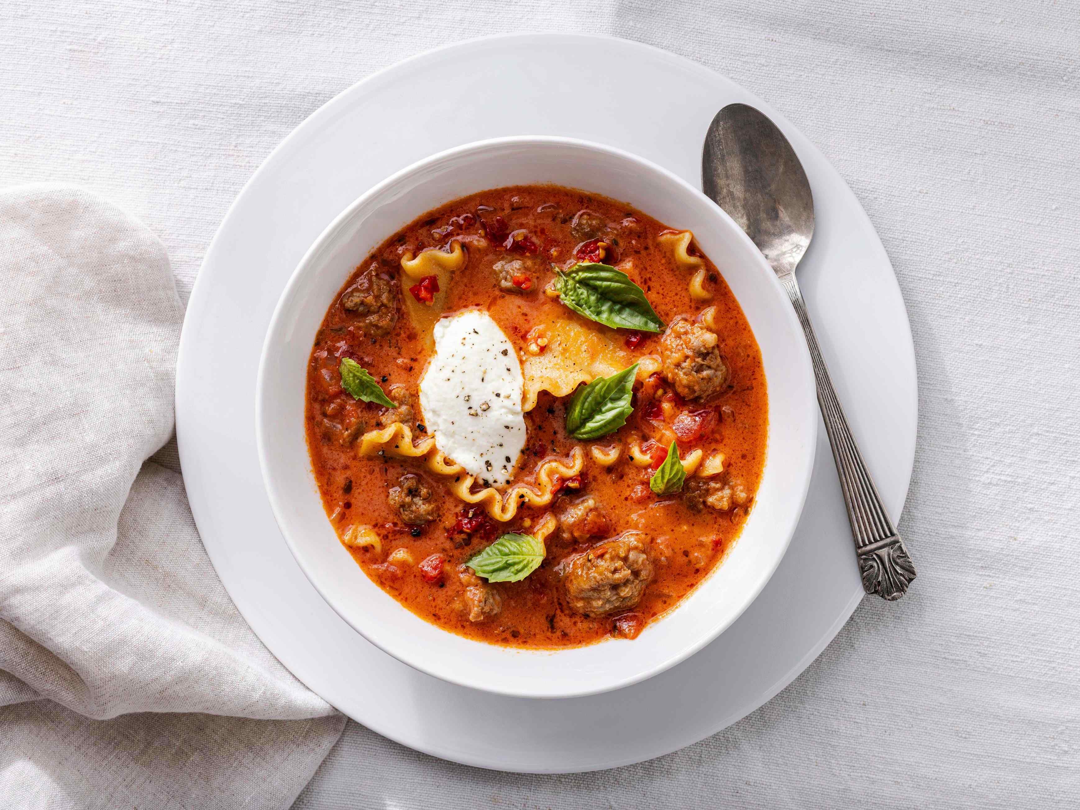 Bowl of soup with lasagna noodles and Italian sausage in broth, topped with dollop of ricotta cheese