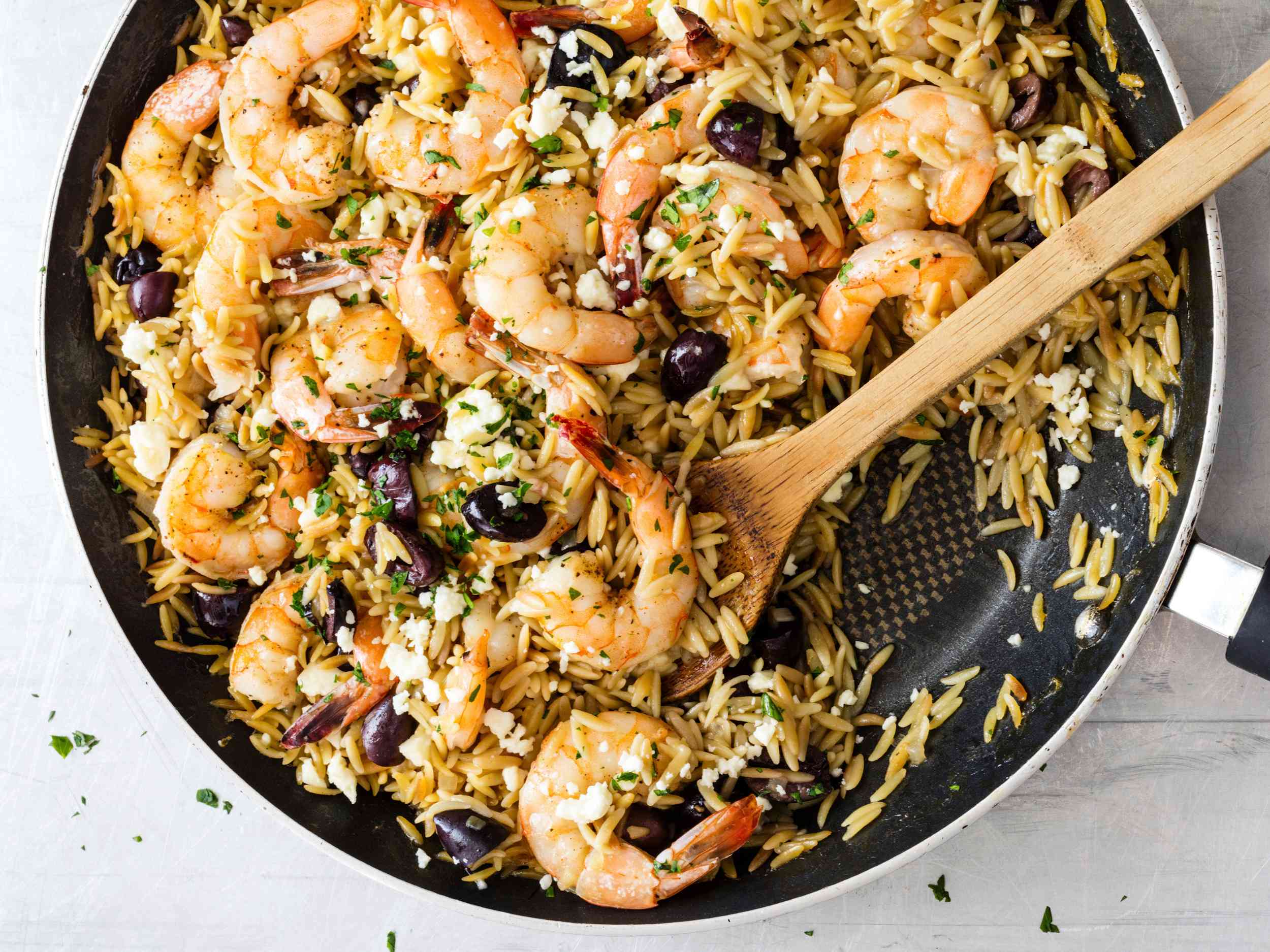 Lemony Shrimp with Orzo, Feta, and Olives in a skillet with a wooden serving spoon