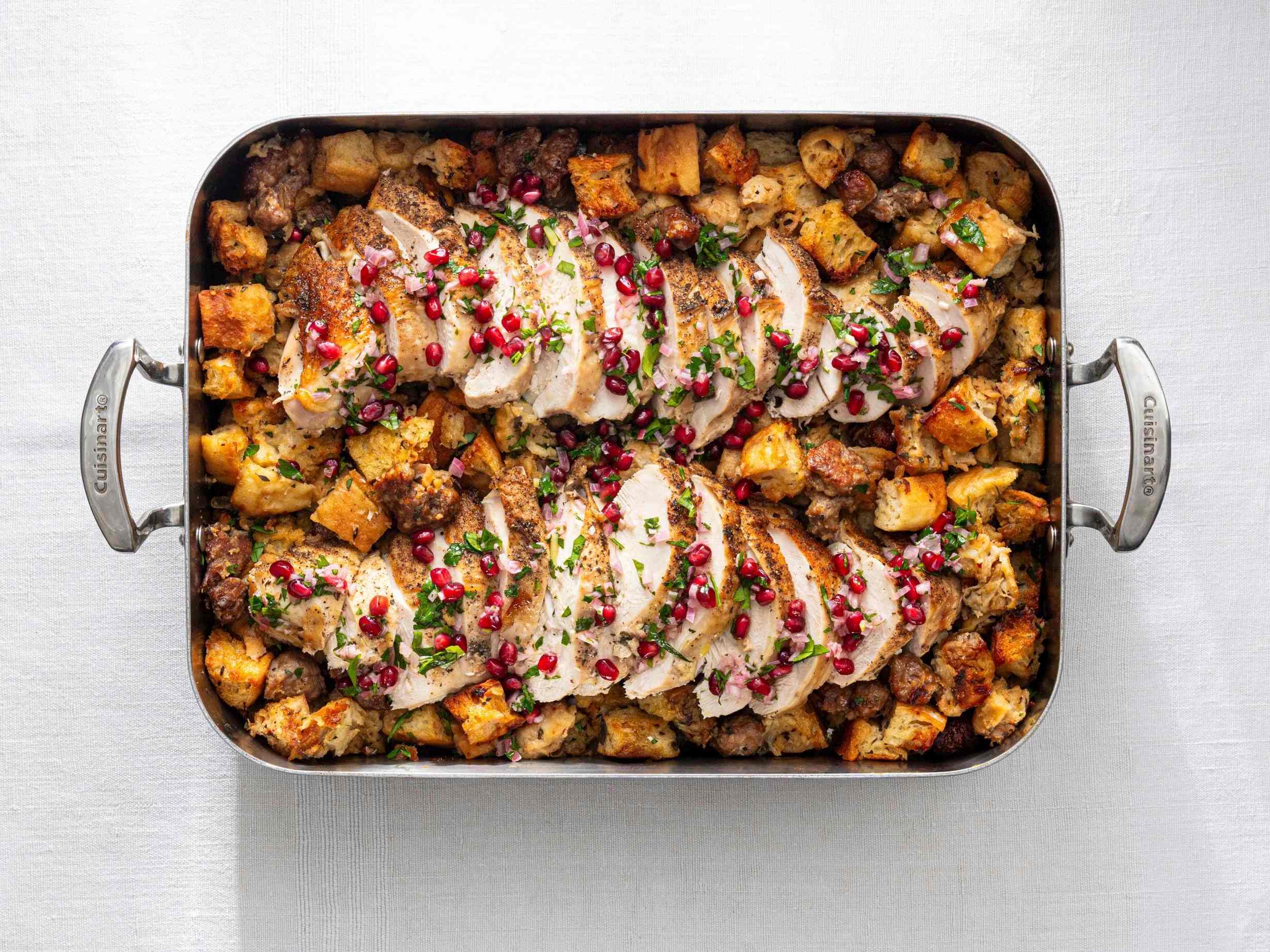 Roasting pan of stuffing with sliced turkey breast over top, sprinkled with pomengranate seed