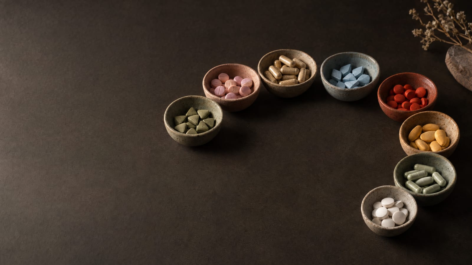 Eight small ceramic bowls in an arc, each holding one kind of pill.
