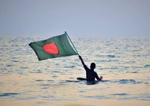 A man waving the Bangladesh flag in the sea at Cox’s Bazar