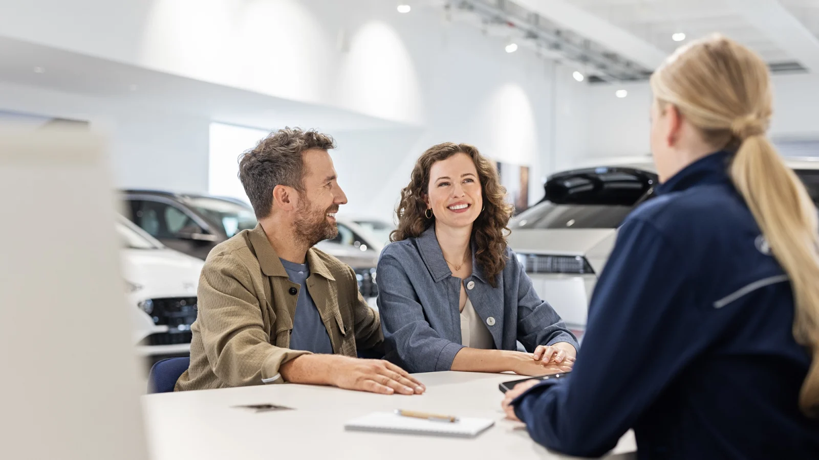 Eine Hyundai Servicemitarbeiterin berät ein Paar an einem Tisch im Verkaufsraum eines Hyundai Partners. 
