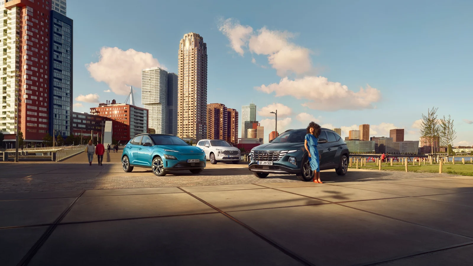 Eine Frau im blauen Kleid lehnt an einen Hyundai TUCSON. Dahinter zwei weitere Hyundai Modelle vor einer Hochhauskulisse.