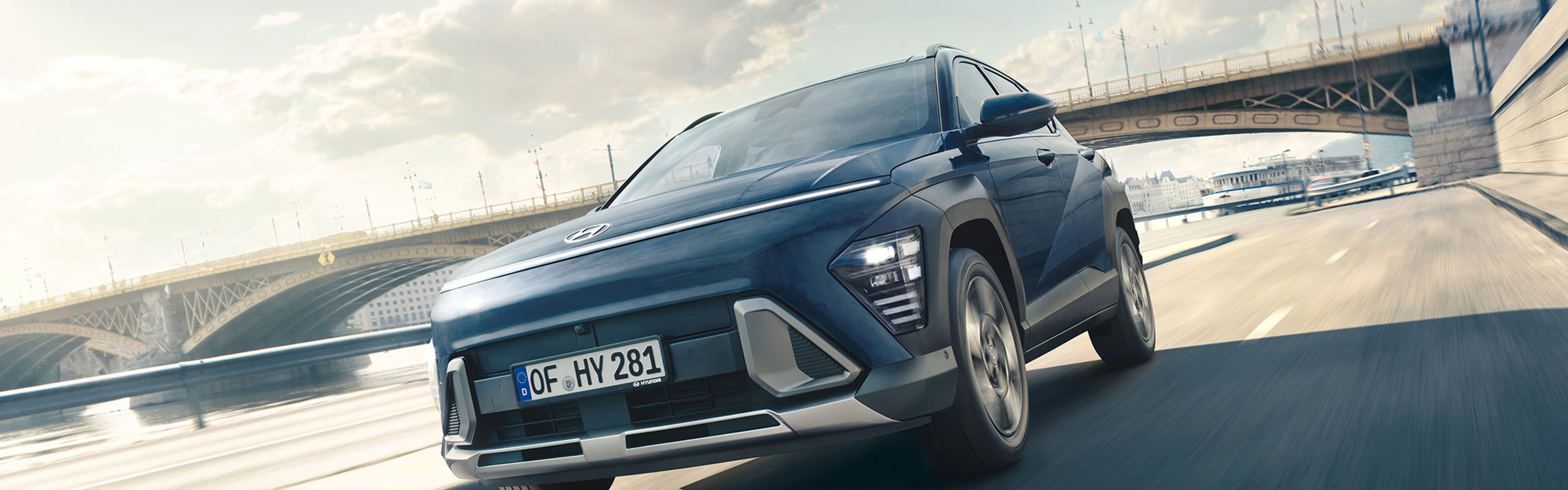 Ein Hyundai KONA Hybrid fährt über eine Brücke, im Hintergrund befinden sich Bürogebäude.