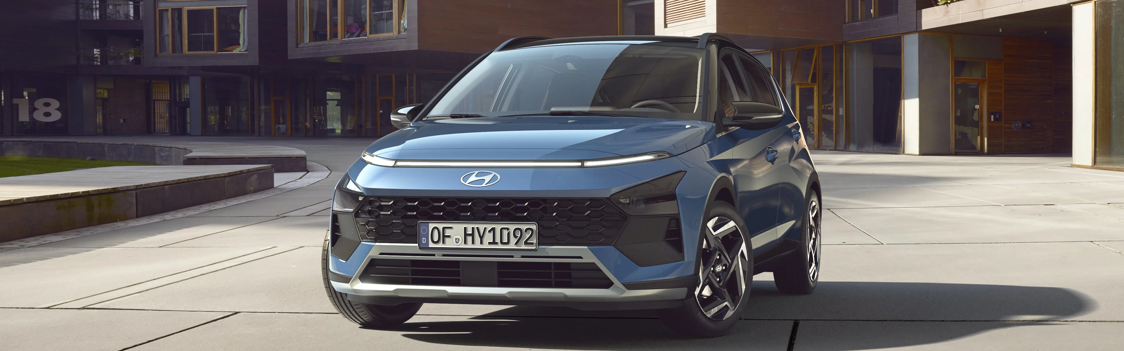 Der Hyundai BAYON, schräg von vorne, vor einem holzverkleideten Bürogebäude.