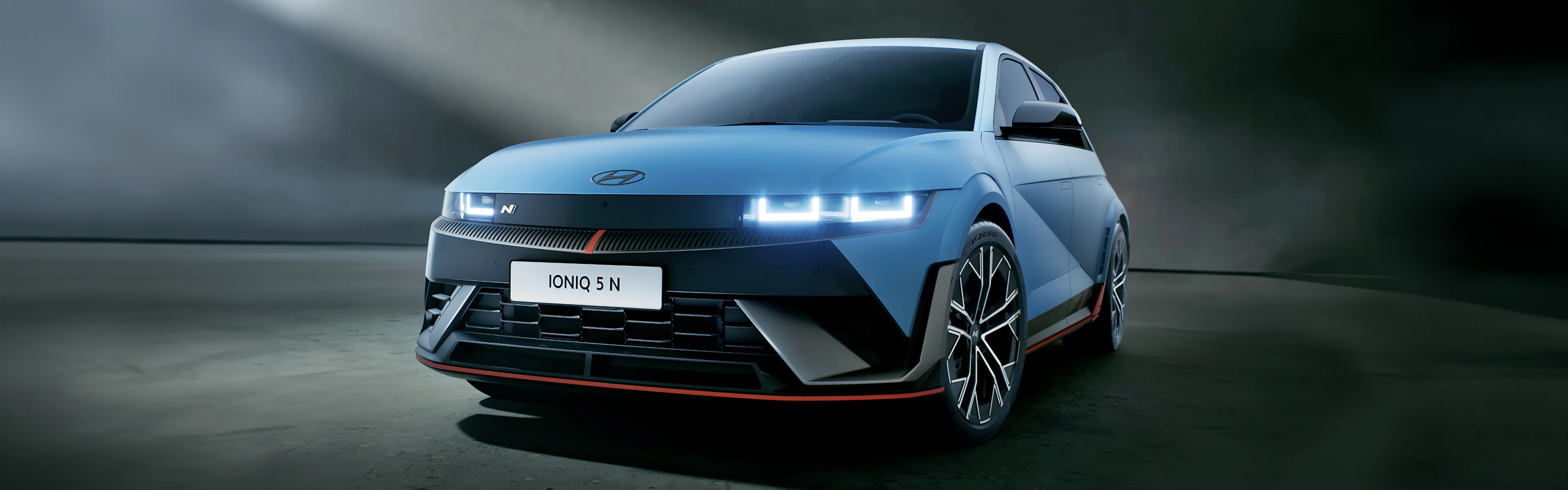 Ein Hyundai IONIQ 5 N in Performance Blue mit angeschalteten Scheinwerfern von schräg vorne.