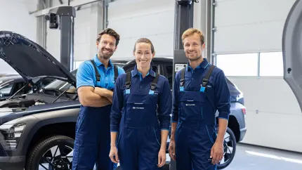 Drei Hyundai Servicemitarbeiter stehen in einer Werkstatt vor einem Hyundai mit geöffneter Motorhaube.