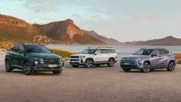 Drei Hyundai SUVs stehen nebeneinander in einer Küstenlandschaft mit Bergen im Hintergrund bei Sonnenuntergang.