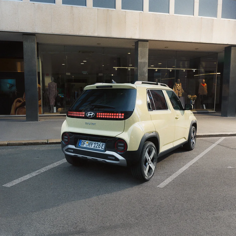 Hellgelber Hyundai INSTER ist rückseitig in einer städtischen Parklücke vor einem Modegeschäft geparkt.