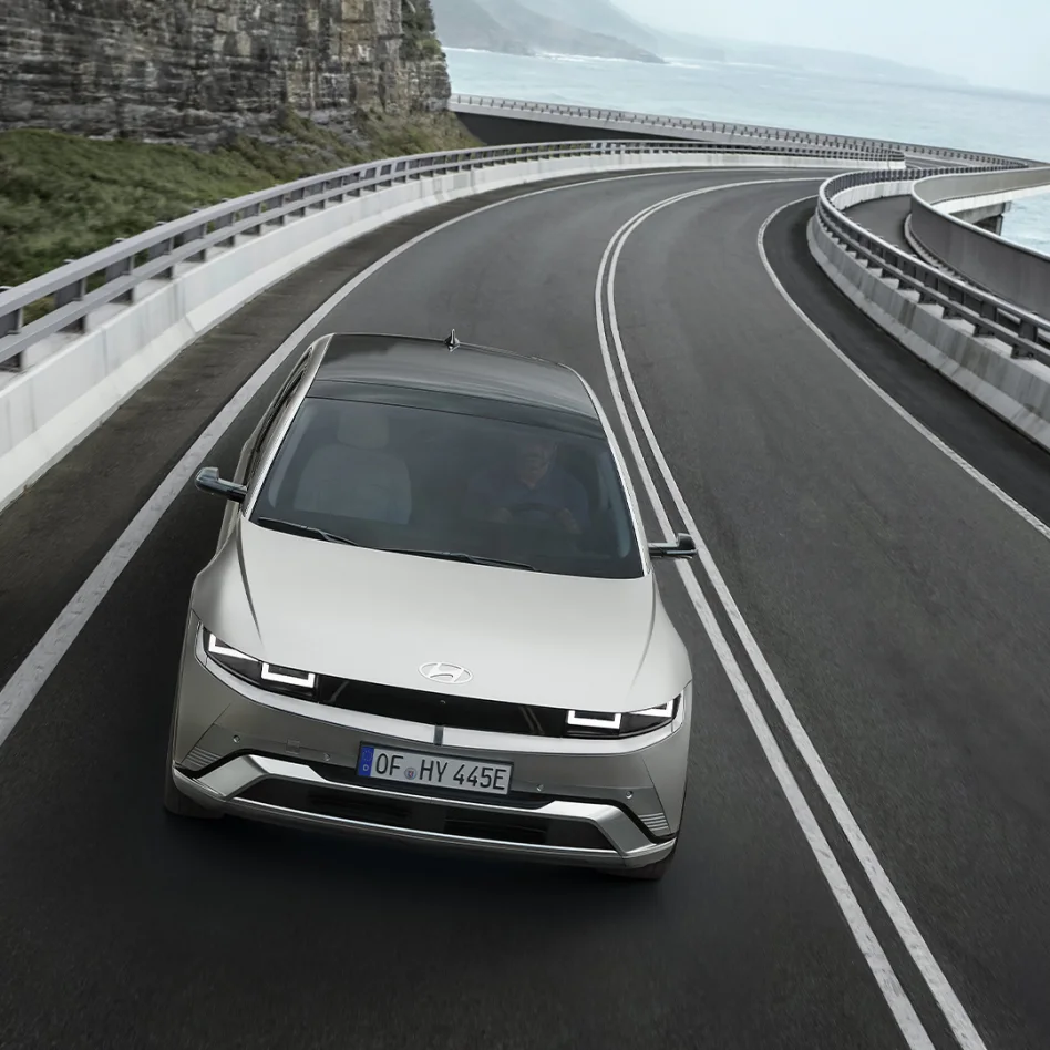 Ein silberner Hyundai IONIQ 5 fährt auf einer kurvigen Küstenstraße entlang einer steilen Felsküste mit Blick aufs Meer.