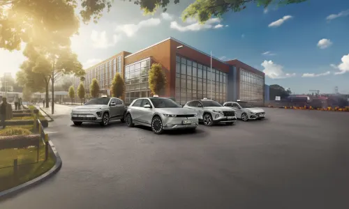 Verschiedene Hyundai Modelle als Fahrschulwagen vor einem modernen Gebäude zwischen einem Park und einer Stadtkulisse.