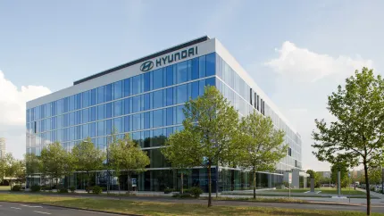 Hyundai Firmengebäude mit Glasfassade. Im Vordergrund: ein Parkplatz mit Bäumen.