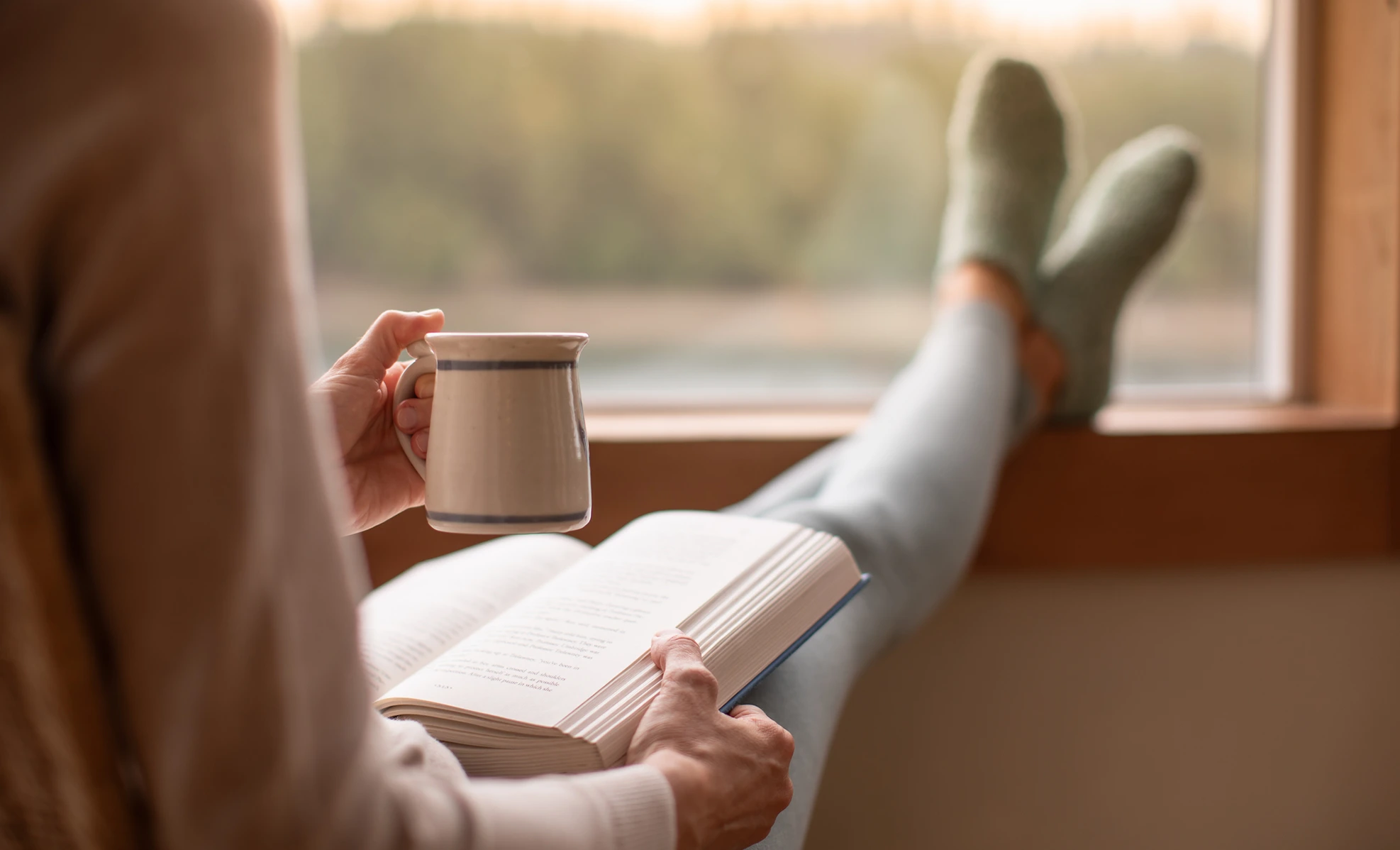Person reading a book by the window on a cold day