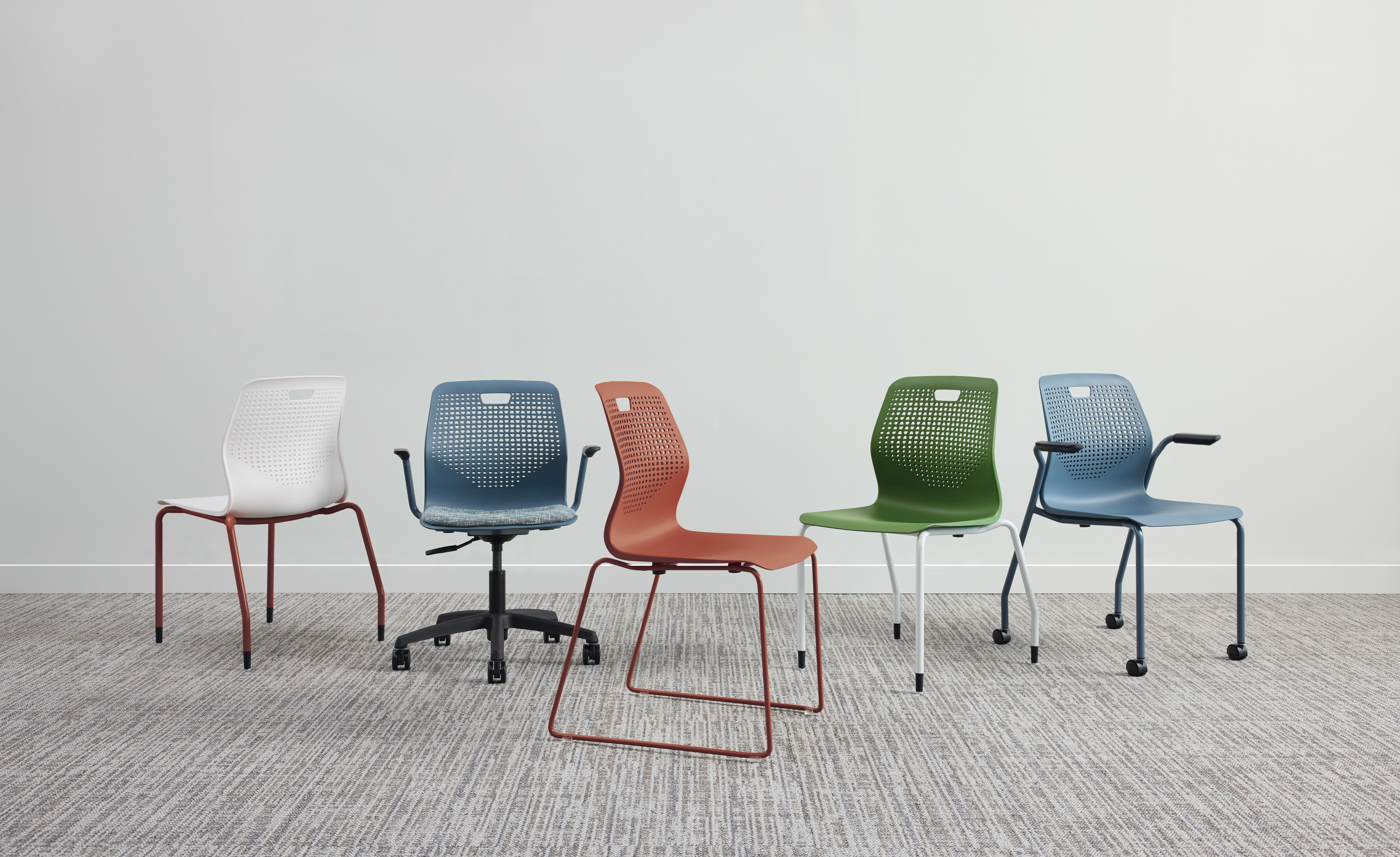 A collection of colorful, modern-looking chairs arranged on a gray tiled floor against a plain white wall.
