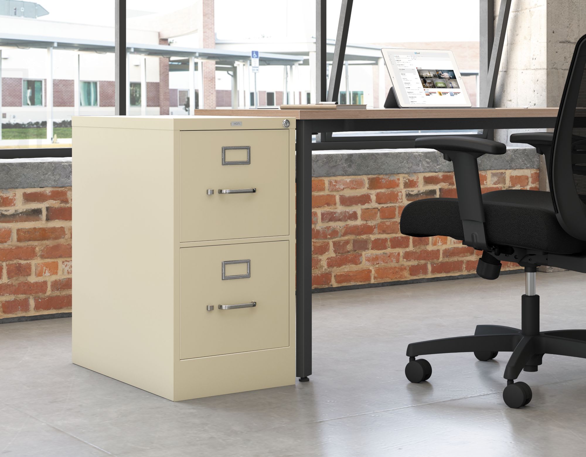 A beige filing cabinet stands in the foreground, with a desk and office chair visible in the background. The walls are made of exposed brick, creating a rustic, industrial atmosphere.