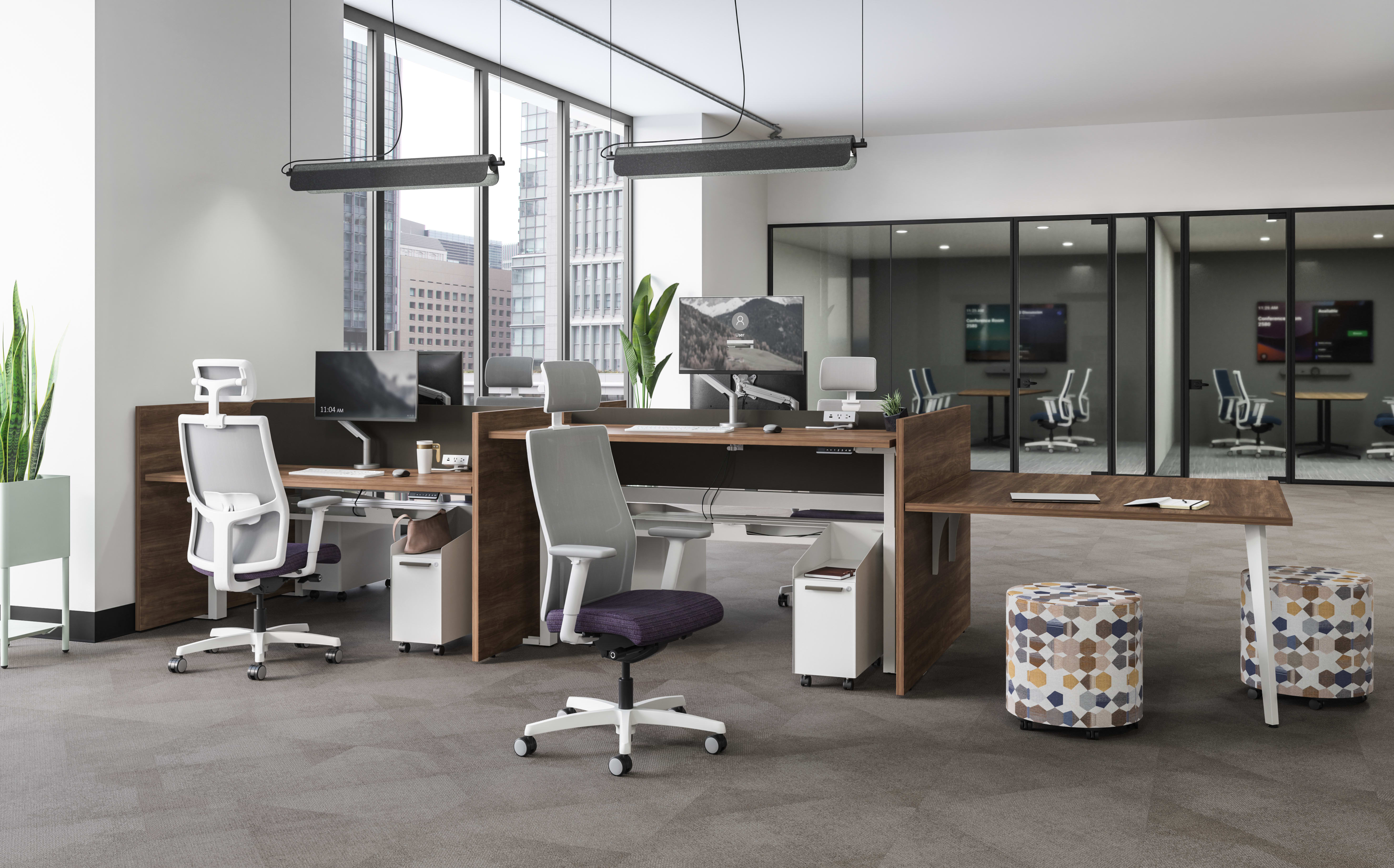 Open office with shared workstations featuring dark wood surfaces, white ergonomic chairs with purple cushions, patterned ottomans, and large windows overlooking a cityscape.