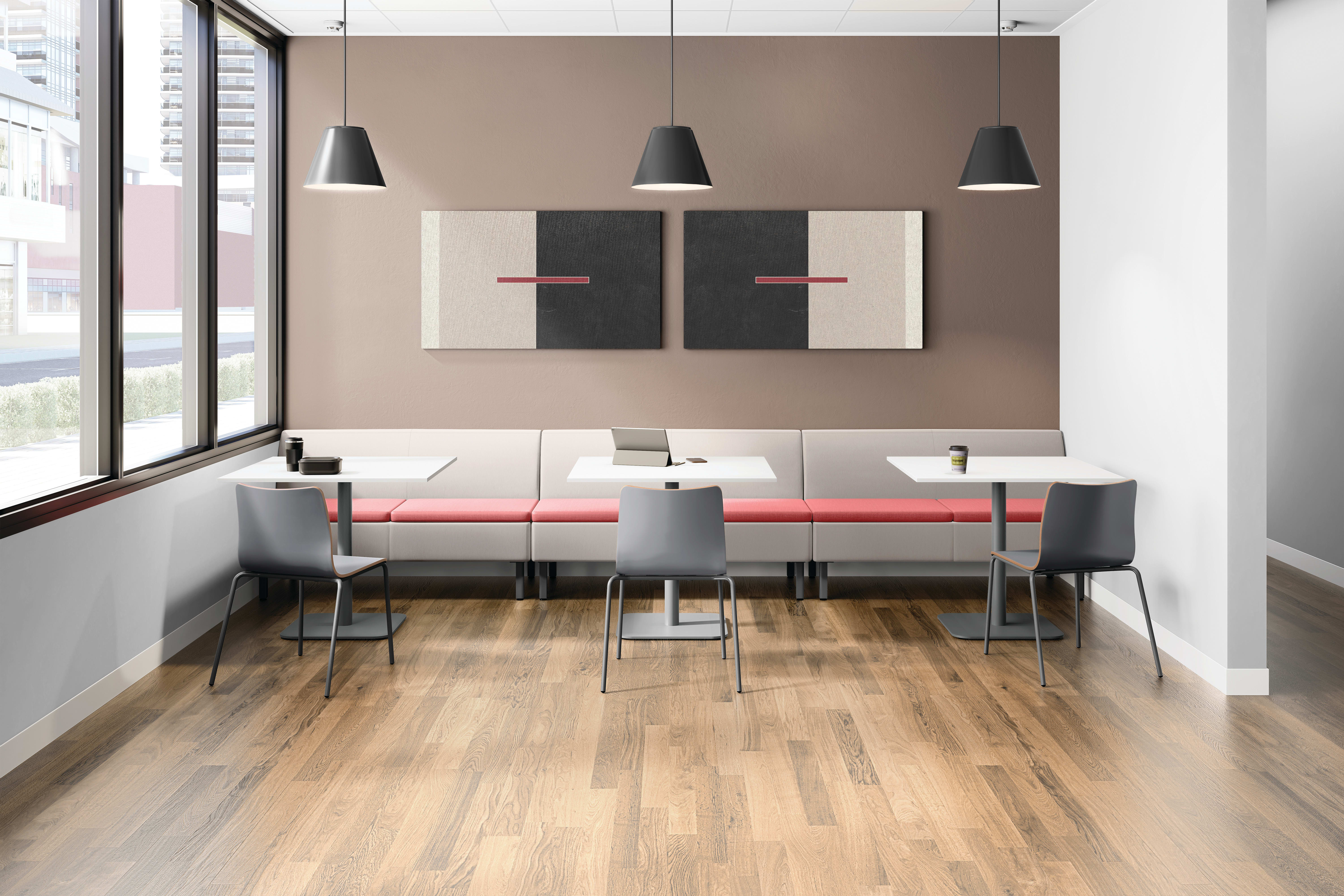 Modern café-style office lounge with bench seating, small tables, side chairs, pendant lighting, wall art, large window, and warm wood flooring in a clean, contemporary setting.