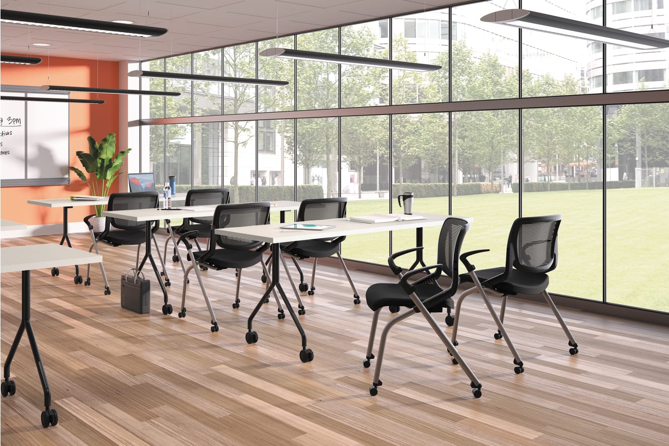 A modern, well-lit classroom with rows of desks and chairs, large windows overlooking a grassy outdoor area, and various lighting fixtures and equipment visible.