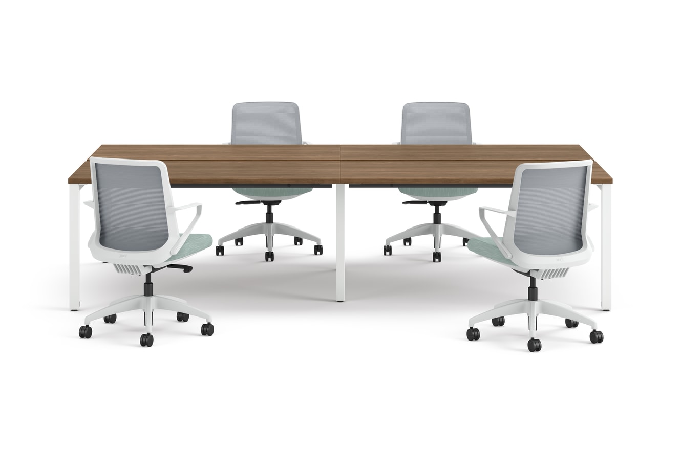 Four ergonomic office chairs arranged around two connected rectangular desks with wooden tops and white legs.