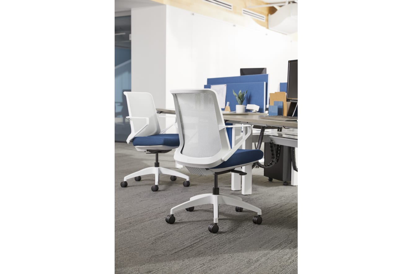 The image shows a modern office space with white and blue office chairs arranged around a table, with shelves and other office equipment visible in the background.