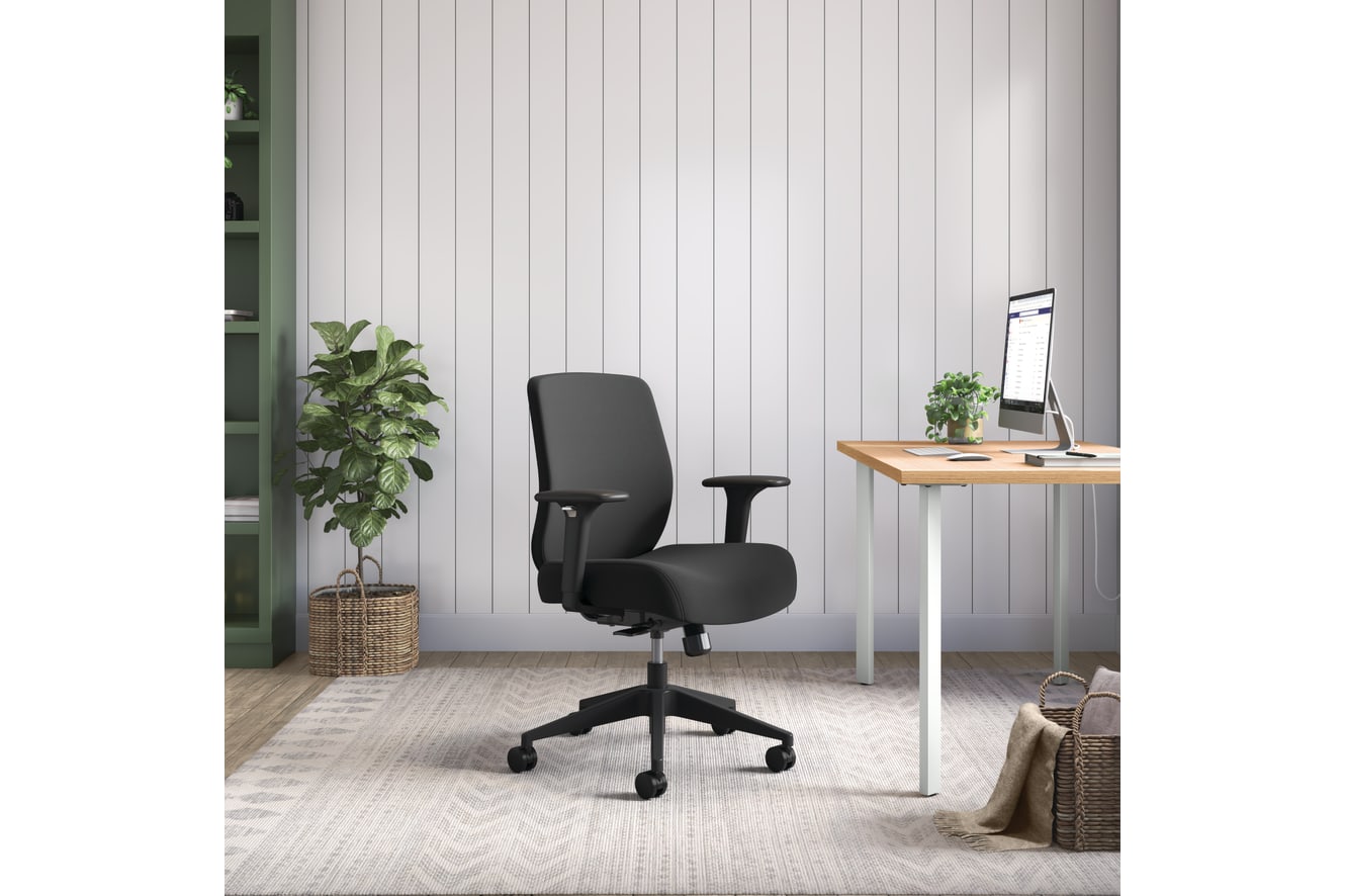 A modern, minimalist home office with a black ergonomic office chair, a wooden desk, and a potted plant in the background.